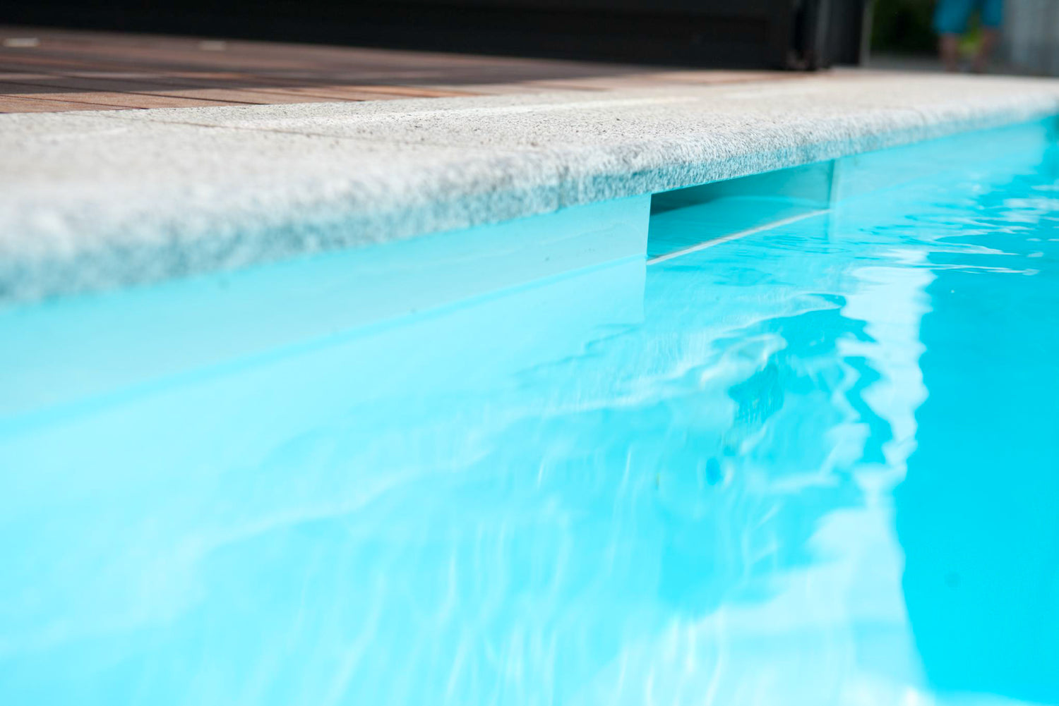 Detailaufnahme eines Pools mit Skimmerkante. Die Wasseroberfläche ist ruhig und klar, das Becken modern gefliest und mit Naturstein umrahmt. Fokus auf hochwertige Verarbeitung und klare Wasserqualität.