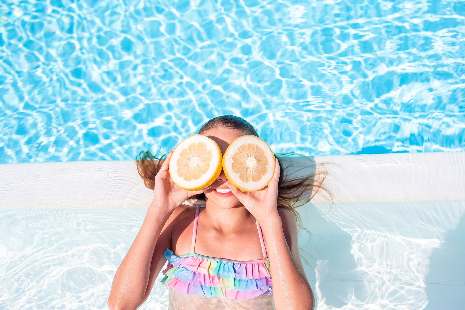 Mädchen im Pool hält zwei Zitronenhälften vor die Augen.